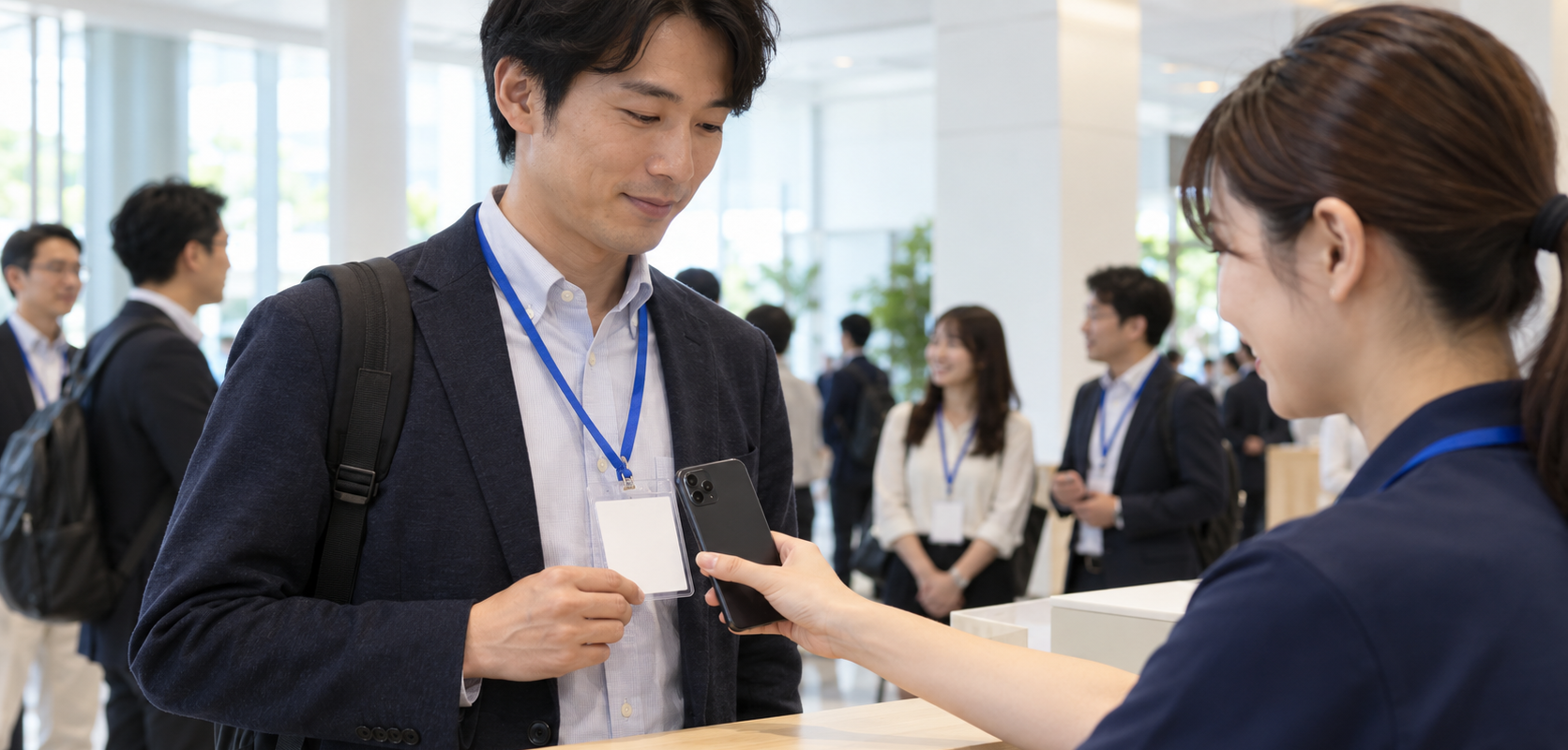 来場者の首掛けカードホルダー内のカードにスマートフォンを近づける受付スタッフ